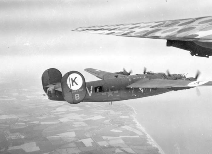 An Army photographer in First Sergeant snaps a photo of a B-24J Liberator of the 458th Bombardment Group climbing out of England and crossing the coast of the English Channel. One look at the dirt and soot on the wing of First Sergeant, and you know she has done her part in the war against the Nazis. Note the waist gunner in the side of Liberator “V”.