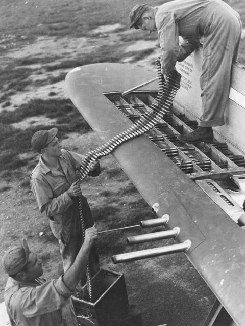 Armorers loading belts of .50 caliber ammunition into the four ammo trays in one wingtip of a P-47 Thunderbolt.