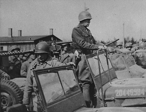 General George Patton (standing in the jeep) prepares to depart from Ohrdruf after an official tour of the newly liberated camp, 1945.