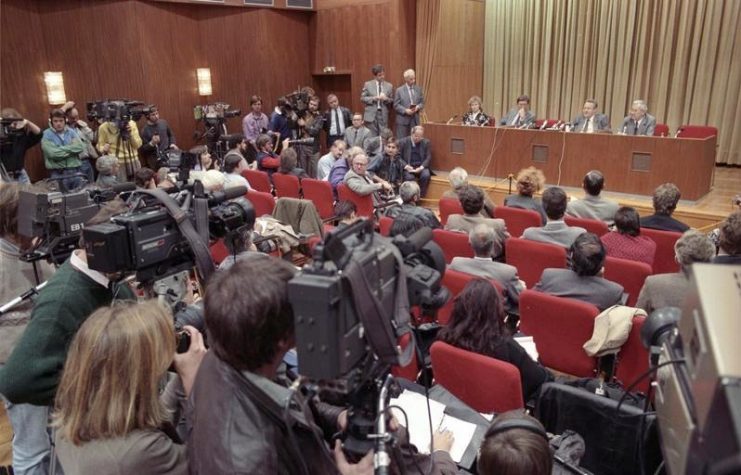 Press conference on 9 November 1989 by Günter Schabowski (seated on stage, second from right) and other East German officials which led to the Fall of the Wall. By Bundesarchiv – CC BY-SA 3.0