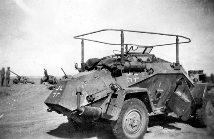 An abandoned German SdKfz 223, Leichter Panzerspähwagen which has been captured by advancing allied troops in North Africa. The vehicle has been fitted with a folding frame antenna for use with a long-range wireless set which is fitted inside the vehicle. Three German 5 cm Panzerabwehrkanone 38 (Pak 38 anti-tank guns) are visible in the background.