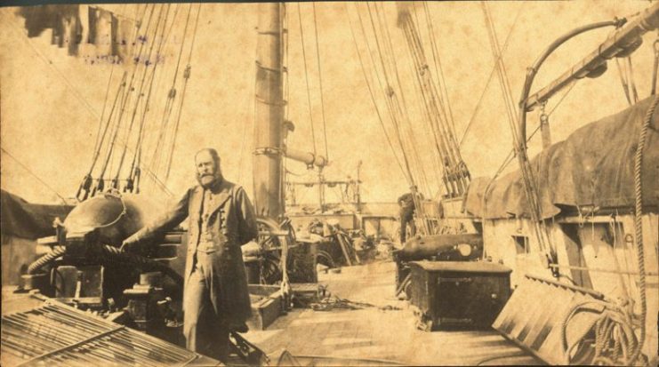 First Lieutenant John McIntosh Kell, who had served with Semmes in his previous command, on the cruiser Sumter, standing by an eight-inch smoothbore gun with his hand on the beech-rope. The engine-room skylight can be seen with bars over the glass. Note the washing hanging in the rigging.