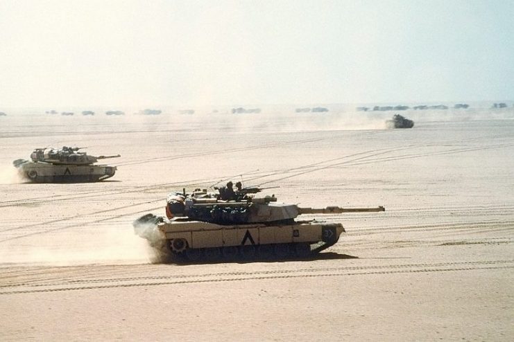 Abrams tanks move out on a mission during Desert Storm in 1991. A Bradley IFV and logistics convoy can be seen in the background.