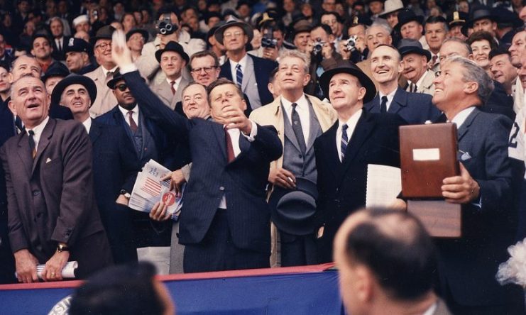 Opening Day of the 1961 Baseball Season. President Kennedy throws out the first ball. (first row) Vice President Johnson, President Kennedy, Dave Powers, Elwood Quesada. (second row) Secretary of HEW Abraham Ribicoff, Assistant Press Secretary Andrew Hatcher, Senator Hubert Humphrey, Senator Everett Dirksen, Senator Mike Mansfield. (third row) Lawrence O’Brien, spectators. Washington, D.C., Griffith Stadium.