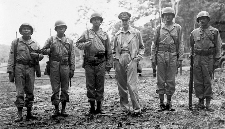 General Douglas MacArthur, commander-in-chief of the Allied forces in the South Pacific, on an inspection trip of American battlefronts, late 1943. From left: Staff Sergeant Virgil Brown (Pima), First Sergeant Virgil F. Howell (Pawnee), Staff Sergeant Alvin J. Vilcan (Chitimacha), General MacArthur, Sergeant Byron L. Tsingine (Diné [Navajo]), Sergeant Larry Dekin (Diné [Navajo]). U.S. Army Signal Corps.
