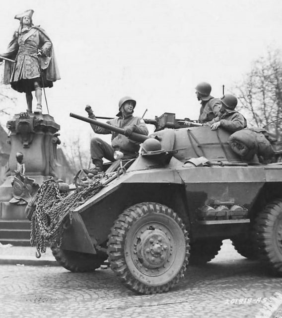 9th Army Troops in M8 passing statue of König Friedrich I in Moers Germany 1945.
