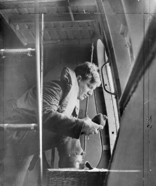 An aircrew sergeant of No. 209 Squadron RAF about to launch a carrier pigeon from the side hatch of a Saro Lerwick flying boat.