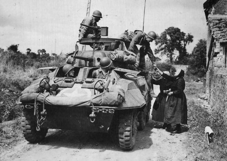 US Troops in M8 stopped by hungry women in Periers 1944.