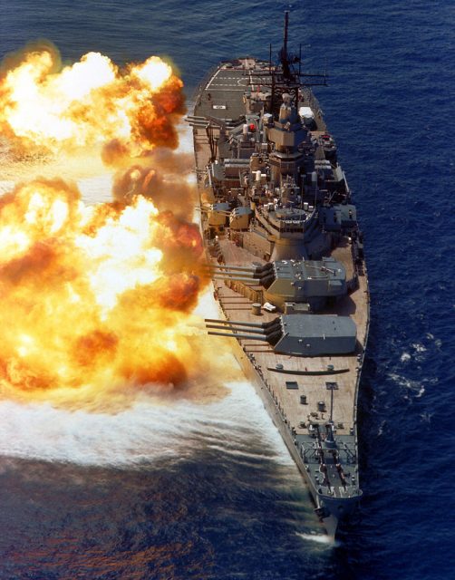 A bow view of the battleship USS IOWA (BB-61) firing its Mark 7 16-inch/50-caliber guns off the starboard side during a firepower demonstration.