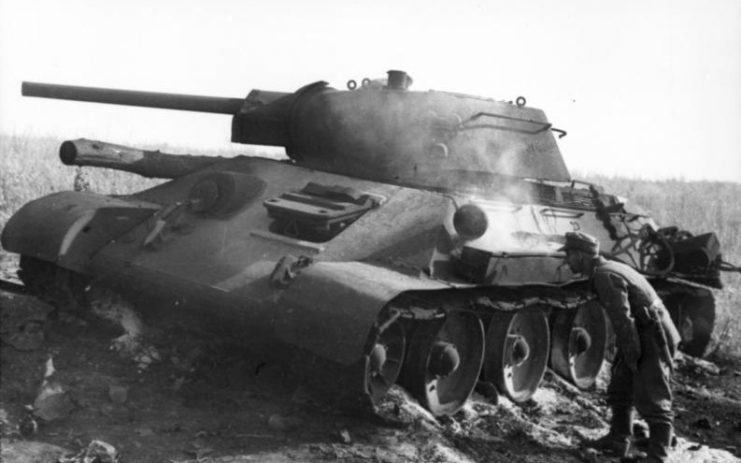 A German soldier inspects a T-34 tank knocked out at Pokrovka that is still smoldering. By Bundesarchiv – CC-BY-SA 3.0