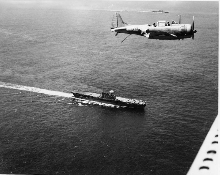 A U.S. Navy Douglas SBD-3 Dauntless flies over the aircraft carriers USS Enterprise (CV-6), foreground, and USS Saratoga (CV-3) near Guadalcanal on 19 December 1942. The aircraft is likely on anti-submarine patrol.