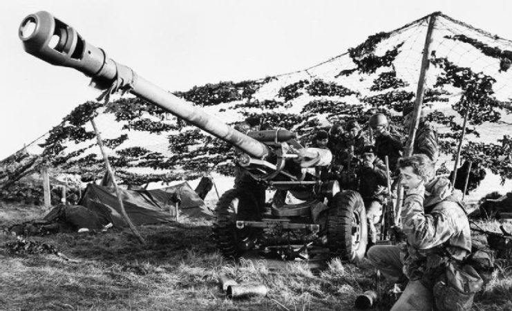 A 105 mm light gun of 29 Commando Regiment, Royal Artillery sited under camouflage netting between Fitzroy and Bluff Cove in the Falkland Islands, June 1982.