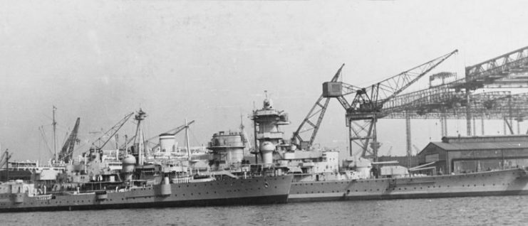 The German heavy cruiser Admiral Hipper, in 1939. The view was taken while the ship was being fitted out at the Blohm & Voss shipyards, Hamburg, Germany, in the spring of 1939. Note the hulk Amazone alongside (left).