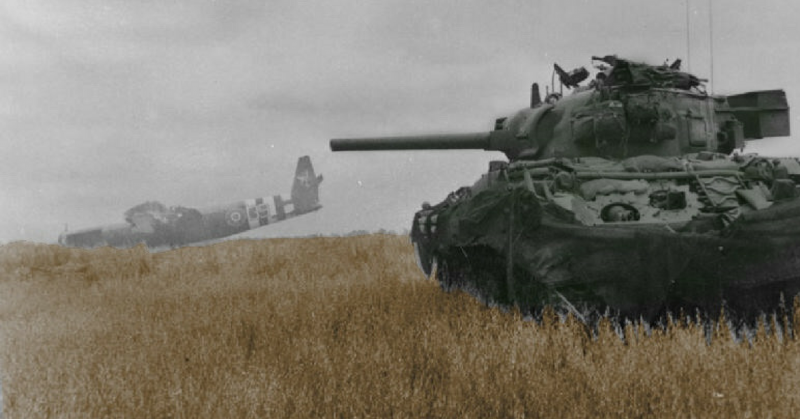 A Sherman tank of 13th/18th Royal Hussars in action against German troops using crashed Horsa gliders as cover near Ranville, 10 June 1944.