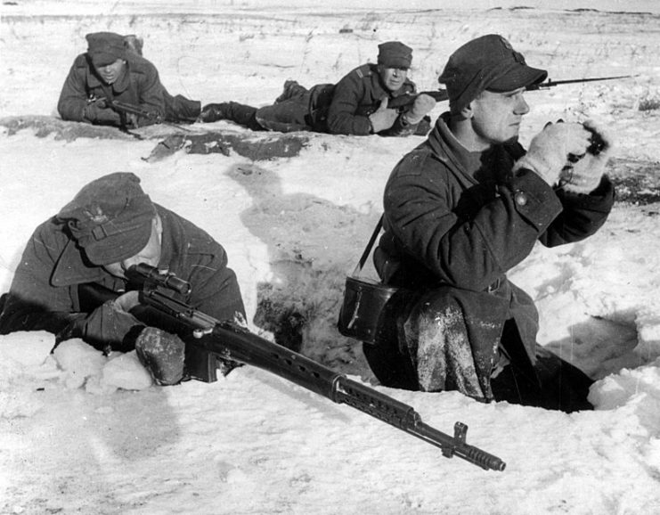 In the foreground a soldier with a SWT-40 rifle equipped with a PU optical sight. Next to an observer with a pair of binoculars. In the background, soldiers with Mosin wz. 38.