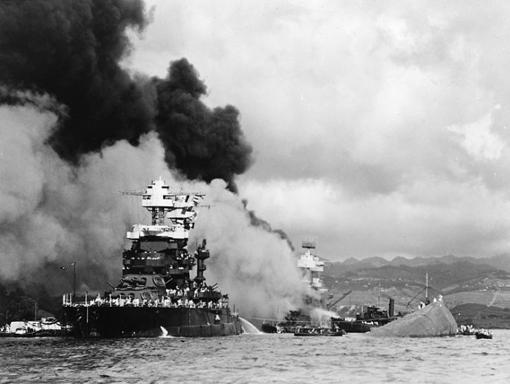 Maryland alongside the capsized Oklahoma during the attack on Pearl Harbor, as West Virginia burns in the background.