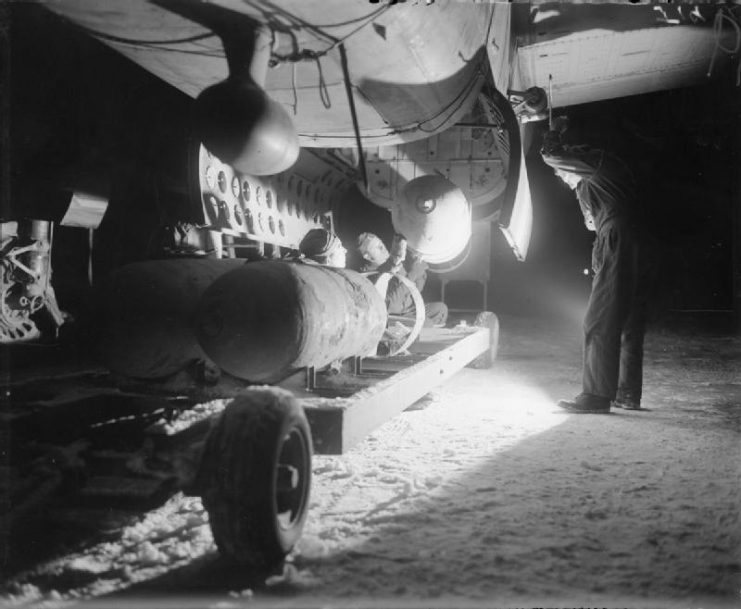 Armorers load four 1,000-lb MC bombs into the bomb-bay of a North American B-25 Mitchell, for an early morning sortie from B58/ Melsbroek, Belgium.