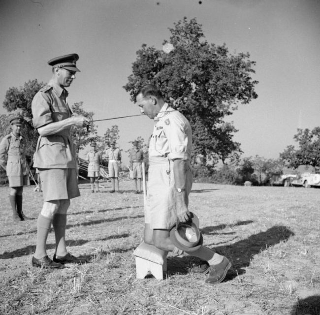 King George VI knights General Sir Oliver Leese in the field.