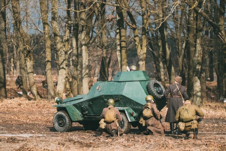 Gomel, Belarus. Group Of Reenactors Dressed As Russian Soviet Red Army Soldiers Of World War II Go On Offensive Under Cover Of Armored Soviet Scout Car Ba-64.