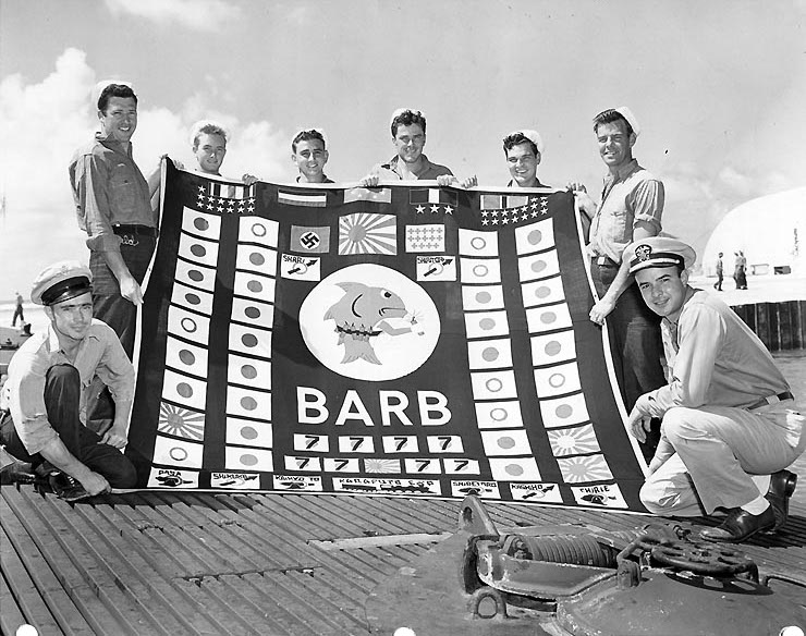 Members of the submarine’s demolition squad pose with her battle flag at the conclusion of her 12th war patrol. Taken at Pearl Harbor, August 1945.