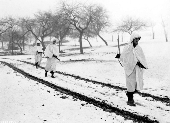 Battle of the bulge – Three members of an American patrol cross a snow-covered Luxembourg field on a scouting mission. White bedsheets camouflage them in the snow.