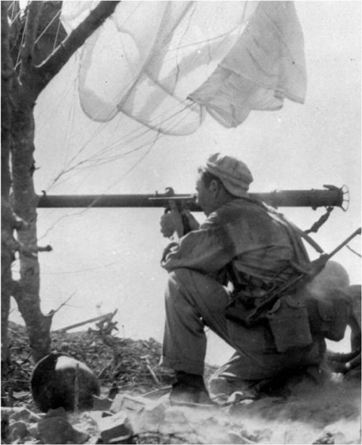 Paratrooper, armed with a U.S. carbine M1A3 with a folding panto-graph stock, fires a bazooka at an enemy pillbox.