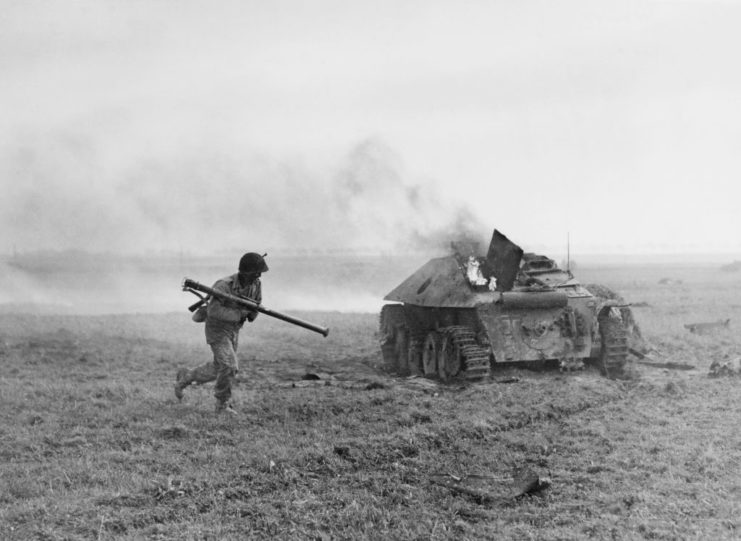 US infantryman armed with a bazooka running past a flaming tank