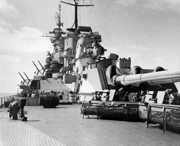 View of the U.S. Navy battleship USS Missouri (BB-63) looking aft towards the number three battery and the superstructure. Note the 20 mm antiaircraft gun mounts in the foreground and the SG surface-search radar antenna atop both mainmasts and the circular antenna for the SK-2 air-search radar on the foremast. Also visible are two Mk 37 gun directors with Mk 12 fire control radar for the 12.7 cm artillery and the Mk 38 gun director with Mk 8 fire control radar (“hedgehog”) for the 40.6 cm artillery.