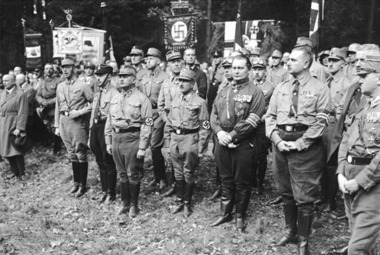Camp service of the NSDAP delegation, in the first row SS Chief Heinrich Himmler, SA Chief Ernst Röhm and Hermann Göring. By Bundesarchiv – CC BY-SA 3.0 de