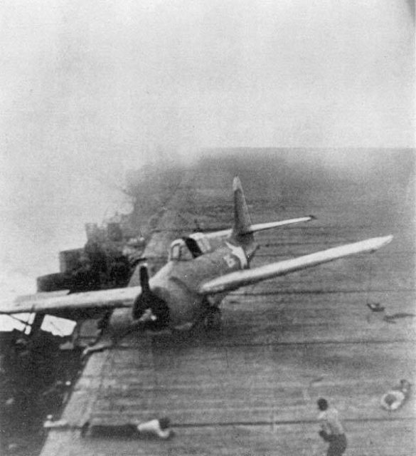 A Hornet Wildcat which had landed on Enterprise slides across the flight deck as Enterprise maneuvers violently under aerial attack on 26 October 1942. Two crewmen are in defensive posture on the deck and the ship appears to be burning.