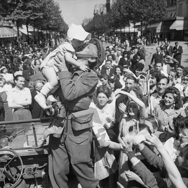An AFPU photographer kisses a small child before cheering crowds in Paris, August 26, 1944
