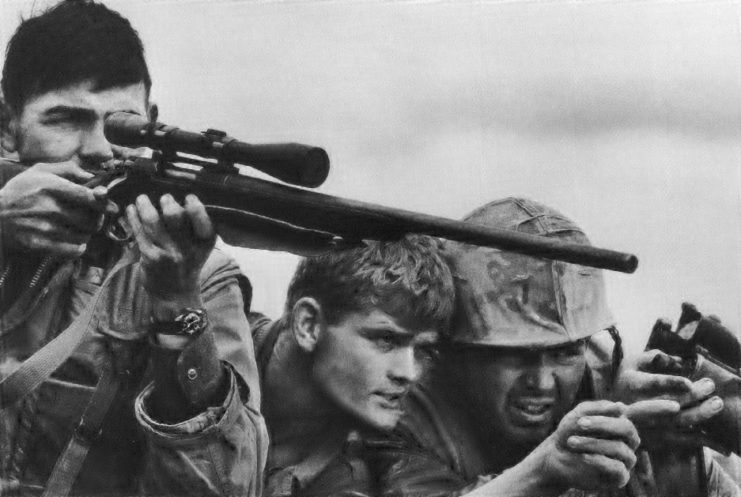 US Marine sniper aiming his rifle while two others point at targets