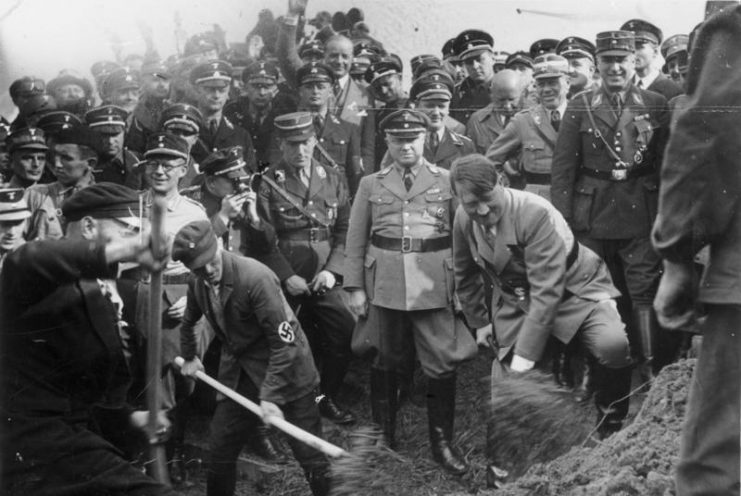 Hitler at a groundbreaking ceremony for a new section of the Reichsautobahn highway system. By Bundesarchiv – CC BY-SA 3.0 de