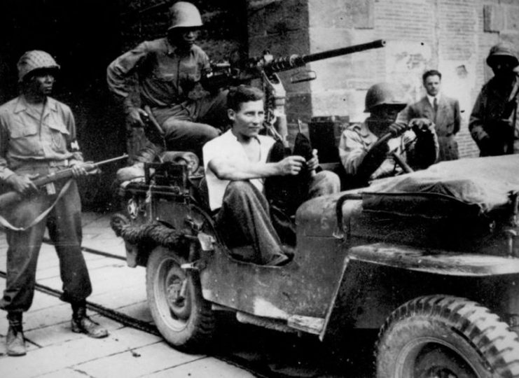 German POW wearing civilian clothes sitting in a jeep at south gate of the walled city of Lucca, Italy, September 1944.