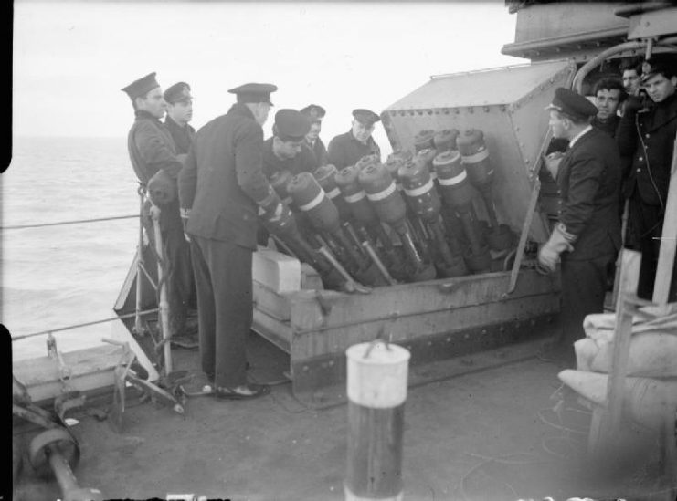 Hedgehog, a 24 spigot anti-submarine mortar. Sailors loading the Hedgehog on board HHMS TOMPAZIS whilst others watch.