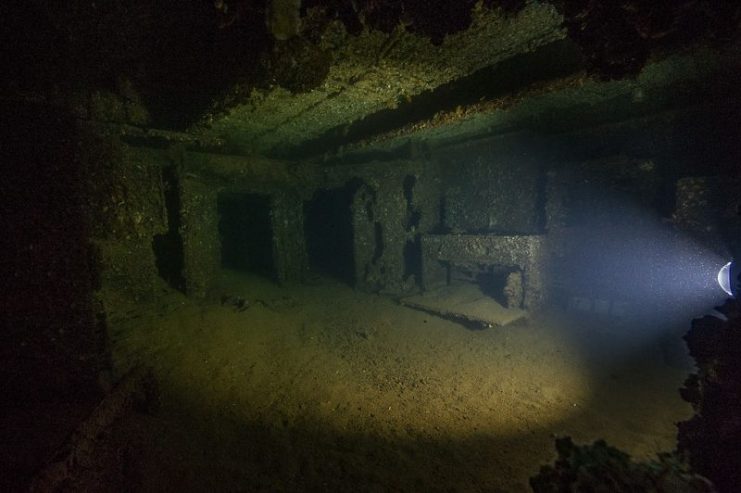 Looking through a porthole into a stateroom of the USS Arizona (BB-39), illuminated by a diver’s light