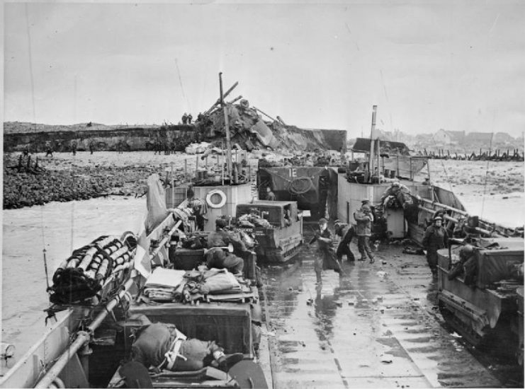 Royal Marine Commandos going down the ramp of a landing craft tank in an Alligator amphibious personnel carrier, whilst some more men in a Weasel amphibious carrier are about to follow.