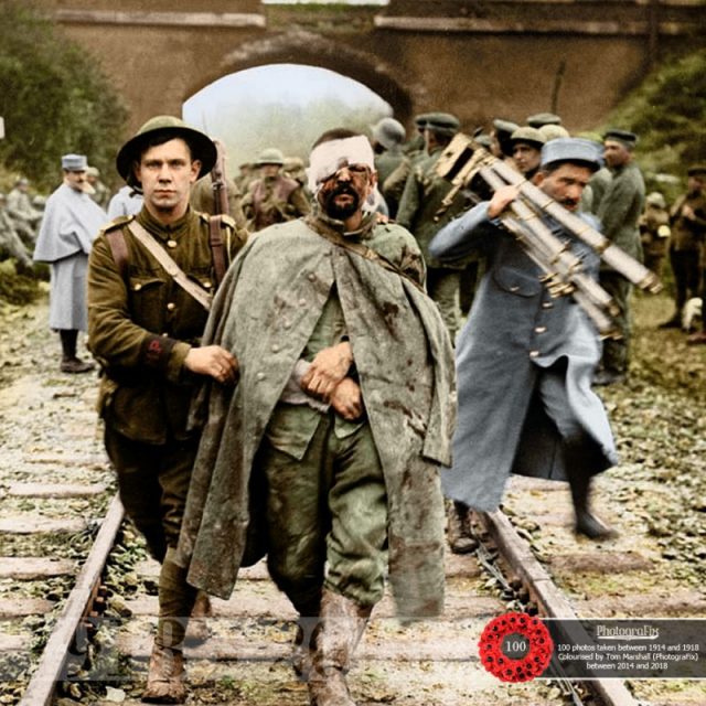 8. Original caption: ‘A Boche prisoner, wounded and muddy, coming in on the 13th.’ A British soldier helps a wounded German prisoner walk along a railway track, 1916. 