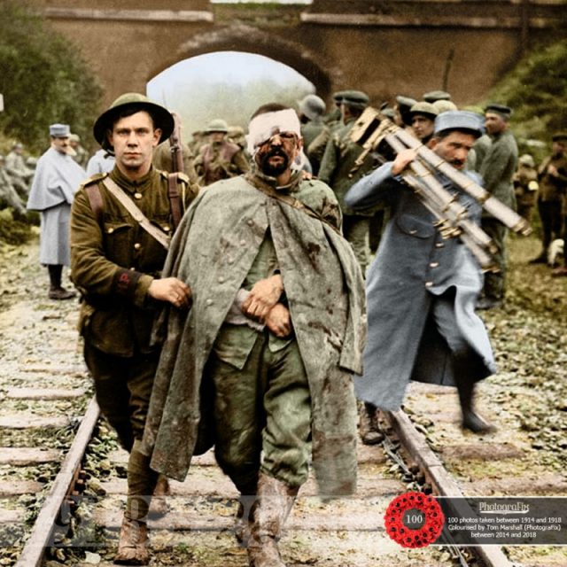 8. Original caption: ‘A Boche prisoner, wounded and muddy, coming in on the 13th.’ A British soldier helps a wounded German prisoner walk along a railway track, 1916.