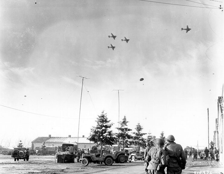 101st Airborne Division troops watch as C-47s drop supplies over Bastogne, 26 December 1944