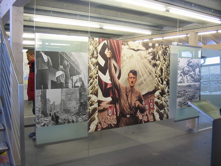 The entrance area of the Obersalzberg Documentation Center displays a well-known propaganda painting by the Führer, framed by photographs of the effects of his Third Reich.Photo: Krischan74 CC BY-SA 3.0