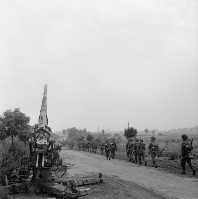 Infantry of 50th (Northumbrian) Division moving up past a knocked-out German 88mm gun near ‘Joe’s Bridge’ over the Meuse-Escaut Canal in Belgium, 16 September 1944