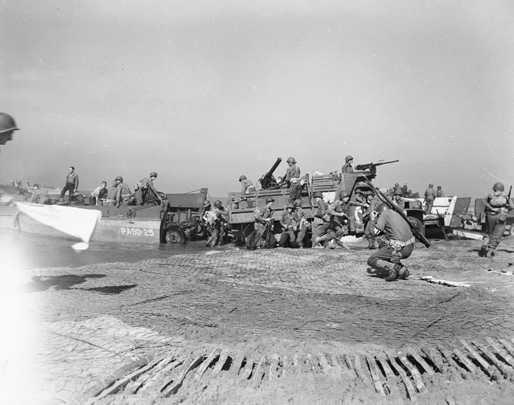 Artillery being landed during the invasion of mainland Italy at Salerno, September 1943. Troops bringing artillery ashore. The MP in the foreground is ducking from a nearby German shell hit.