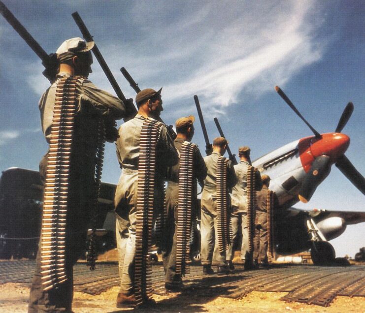 Crewmen lining up in front of a North American P-51 Mustang with ammunition belts slung over their shoulders