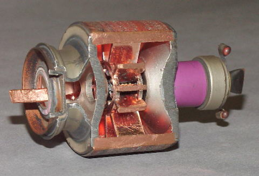 Magnetron with section removed to exhibit the cavities. The cathode in the center is not visible. The waveguide emitting microwaves is at the left. The magnet producing a field parallel to the long axis of the device is not shown.Photo: HCRS CC BY-SA 2.0