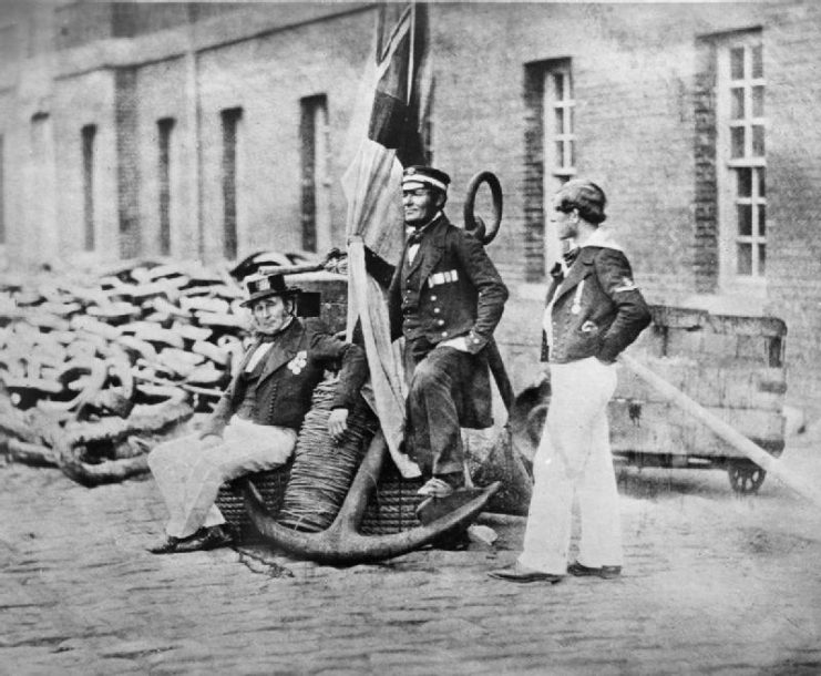 Royal Navy seamen who served in the Crimea: Admiral’s Coxswain Charles Brooks, HMS BRITANNIA; Boatswain John Starling, HMS SAMPSON; Leading Seaman W Pengelly, HMS SANSPAREIL, pose with an anchor and Royal Navy ensign.