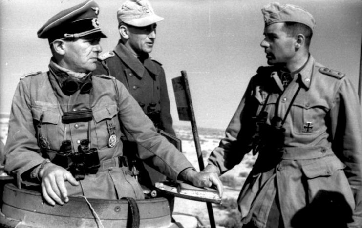 Three German officers confer together atop a tank in North Africa.