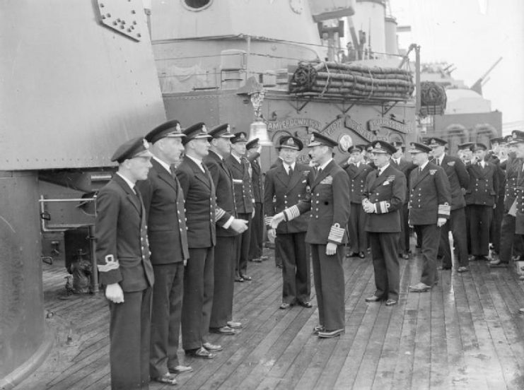 HM King George VI meeting the officers of HMS London lined up on deck next to one of the cruiser’s 8-inch gun turrets, part of the Home Fleet at Scapa Flow.