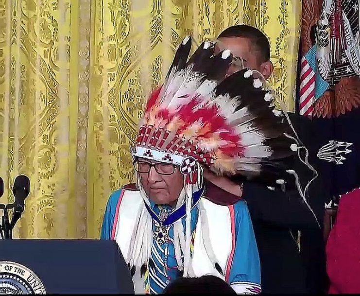 Joseph Medicine Crow-High Bird at the 2009 Medal of Freedom ceremony, the award is seen around his neck and President Obama is behind him, securing the award.