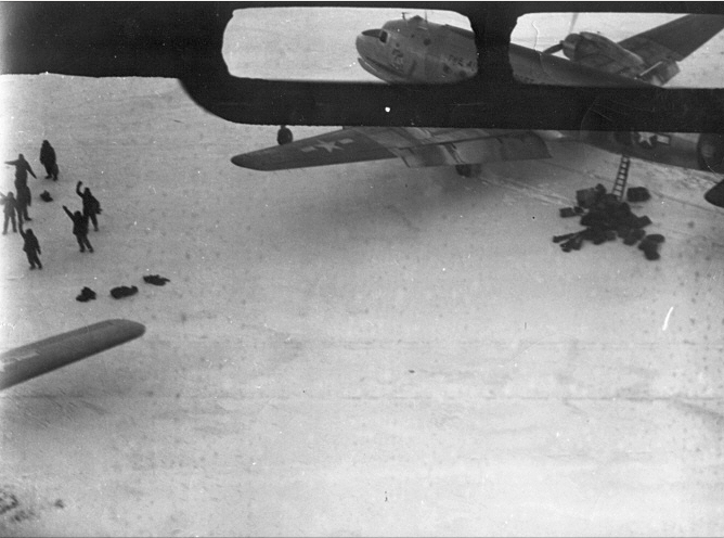 The Kee Bird rescue. C-54 rescue plane is soon preparing to pick up the aircrew, shown on the ice waving to the photo plane flying over. The boarding ladder is in place, and take-off from the crash site is imminent.